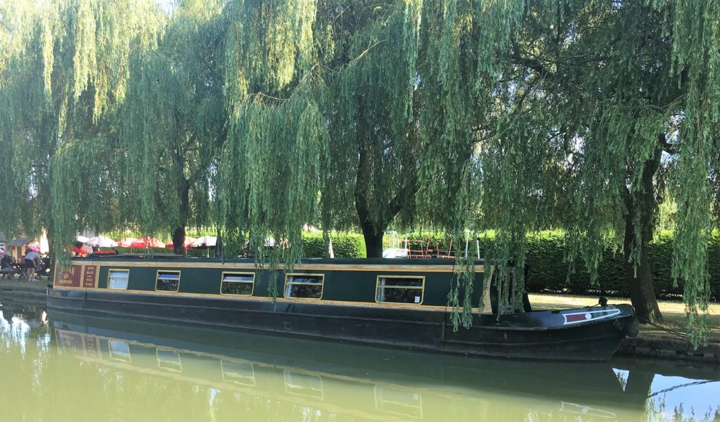 Narrowboat moored by the pub, under overhanging willows